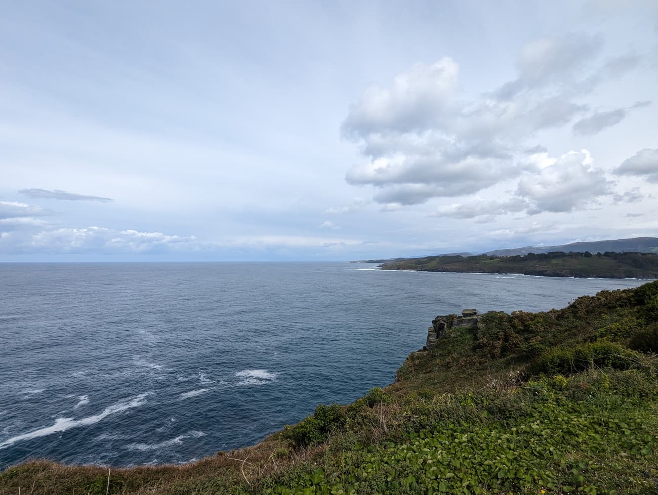 Green clifftop above the Bay of Biscay, the Asturian coastline receding in headlands under a broken grey sky.