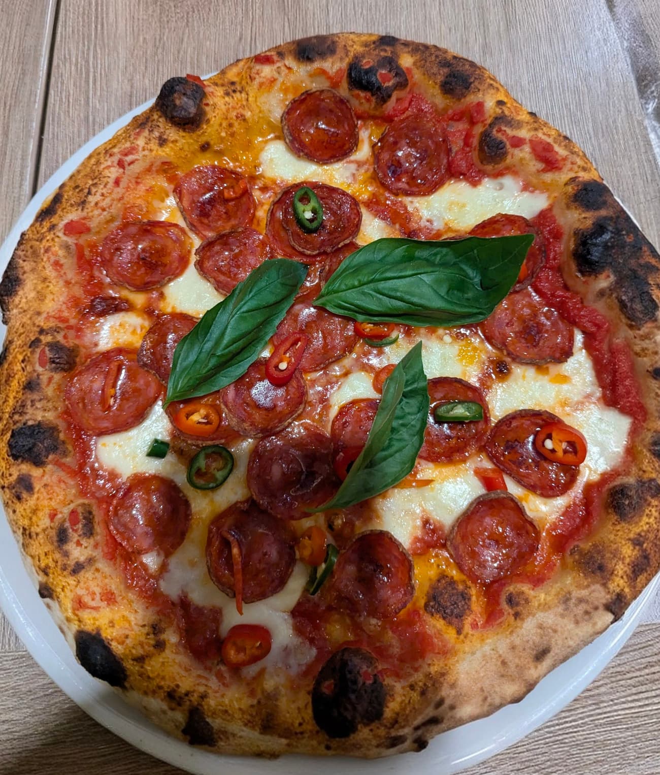 A wood-fired pizza with a blistered leopard-spotted crust, spicy salami, sliced red and green chillies and fresh basil.