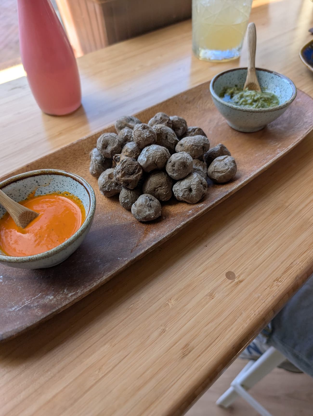 Papas arrugadas — salt-crusted wrinkled potatoes — on a wooden board between bowls of red and green mojo with little wooden spoons.
