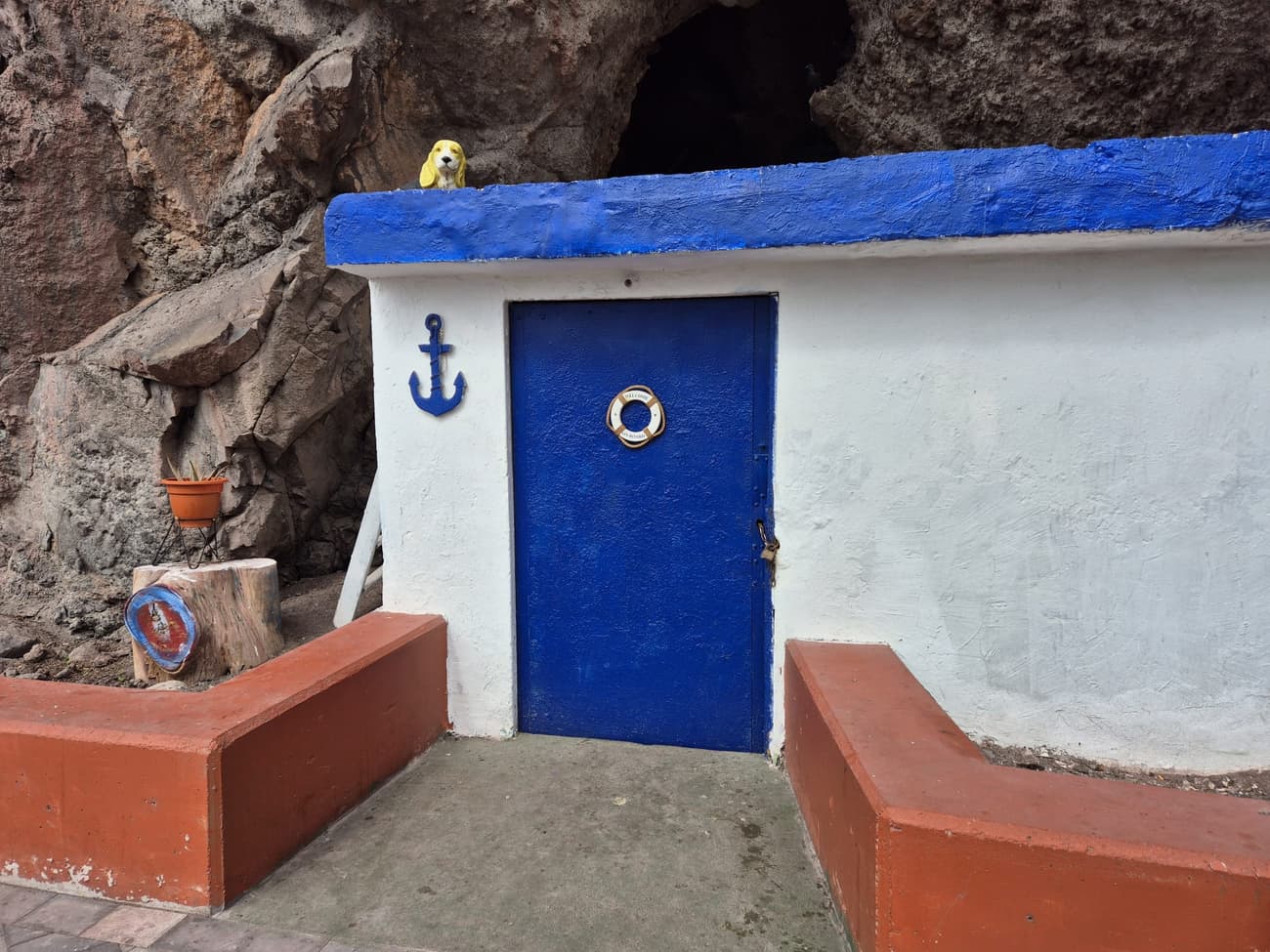 A tiny blue-and-white fisherman's hut built into the volcanic rock, a painted anchor and a 'welcome on board' lifebuoy on the wall and a ceramic dog on the roof.