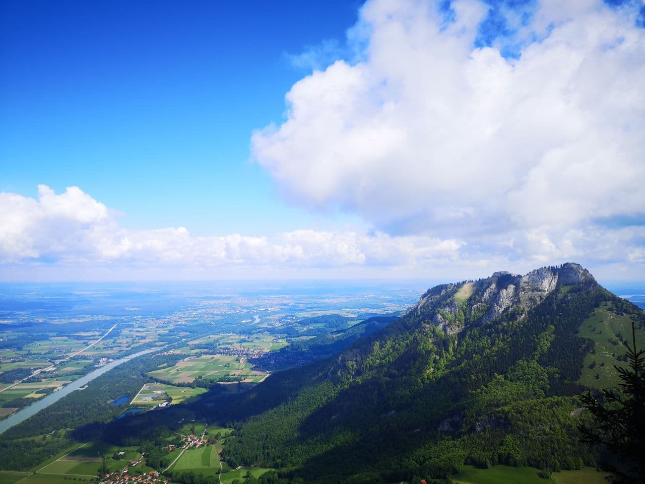 View from the Kranzhorn over the Inn valley, the river winding between fields and villages, the rocky summit ridge falling away to the right.