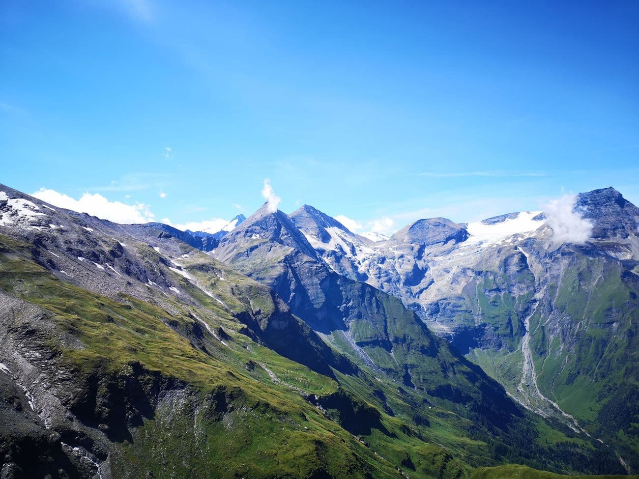 A glaciated range with snowfields and a glacier tongue spilling between rock walls, green pasture in the foreground.