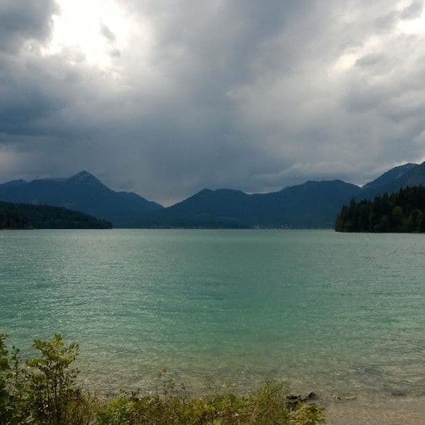 The turquoise water of the Walchensee under heavy grey cloud, forested mountains ringing the far shore.